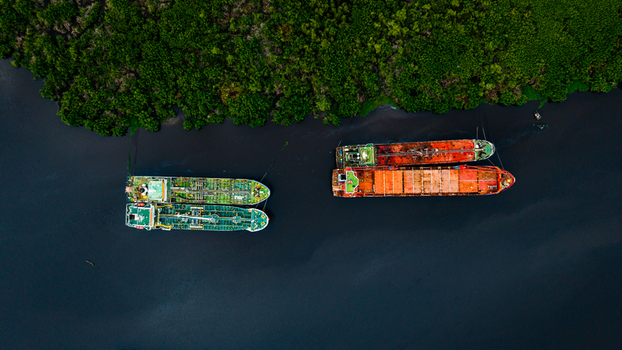 Aerial view of cargo ships moored in the dark waters of a river lined with dense green mangroves in Lagos Lagos Nigeria.
