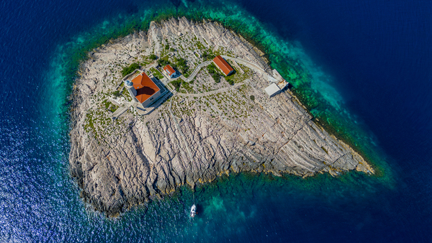 Aerial view of Blitvenica Lighthouse on a small rocky island with a boat anchored in the turquoise and blue Adriatic Sea in Zirje Sibensko kninska zupa Croatia. Aerial view of Blitvenica Lighthouse on a small rocky island with a boat anchored in the turquoise and blue Adriatic Sea in Zirje Sibensko kninska zupa Croatia.