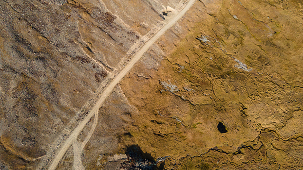 Aerial view of the rugged landscape of Deosai Plains with a dirt road cutting through the golden brown terrain and small streams in Skardu Gilgit Pakistan.