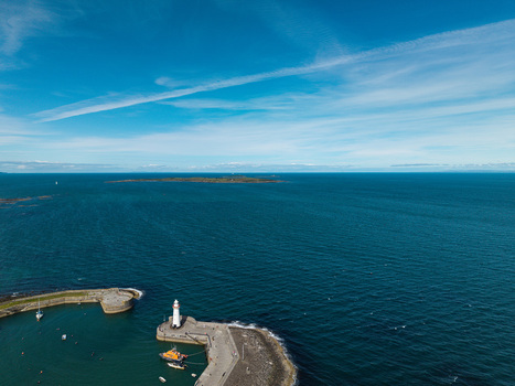 Aerial view of Donaghadee Harbour with its iconic lighthouse stone breakwater and calm blue sea under a clear sky in Donaghadee Northern Ireland United Kingdom. Aerial view of Donaghadee Harbour with its iconic lighthouse stone breakwater and calm blue sea under a clear sky in Donaghadee Northern Ireland United Kingdom.