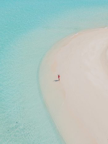 Aerial view of a lone figure standing on the pristine white sands where the turquoise waters meet Vashafaru Island Thiladhummathi Atoll Maldives.