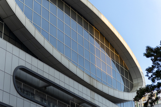 View of the modern curved glass facade and sleek metal panels of a contemporary building under a clear blue sky Taipei City Taiwan. View of the modern curved glass facade and sleek metal panels of a contemporary building under a clear blue sky Taipei City Taiwan.