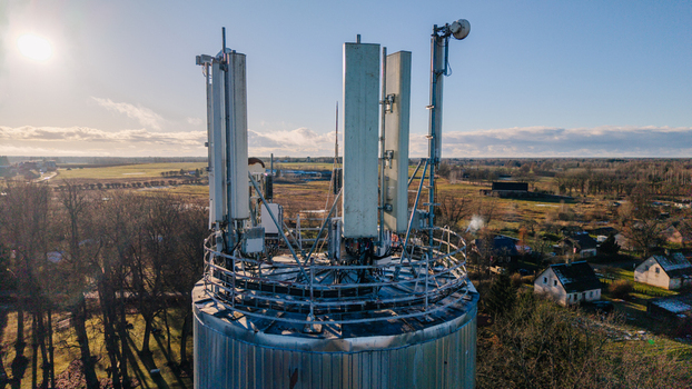 Valmiera Latvia 11 November 2025 Aerial view of a telecommunications tower with antennas and satellite dishes set against a rural landscape under a clear sky.