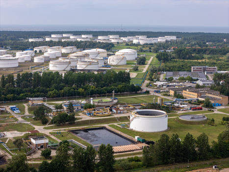 Aerial view of an industrial oil storage facility with large white tanks pipelines and processing units surrounded by green vegetation in Gdansk Pomeranian Voivodeship Poland. Aerial view of an industrial oil storage facility with large white tanks pipelines and processing units surrounded by green vegetation in Gdansk Pomeranian Voivodeship Poland.