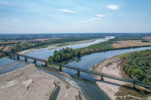 Aerial view of the historic Ponte della Becca iron bridge spanning the Po river with dry sandy banks and green vegetation in Linarolo Lombardia Italy.