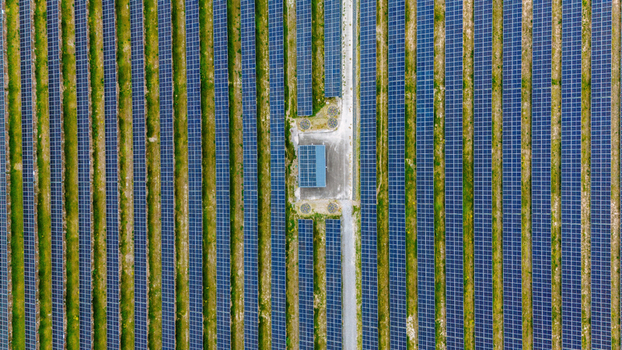 Aerial view of rows of blue solar panels installed in a green field with a central control building Sabac Vojvodina Serbia.