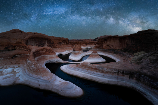View of Reflection Canyon with its winding sandstone walls and dark water under a clear starry night sky with the Milky Way Kane County Utah United States. View of Reflection Canyon with its winding sandstone walls and dark water under a clear starry night sky with the Milky Way Kane County Utah United States.