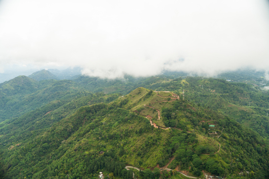 View of lush green hills and a winding mountain road leading through the landscape under a cloudy sky in Gampola Central Province Sri Lanka. View of lush green hills and a winding mountain road leading through the landscape under a cloudy sky in Gampola Central Province Sri Lanka.
