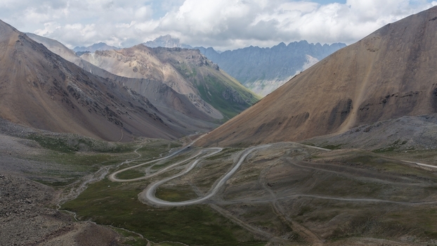 Aerial view of the winding mountain road through the Enilchek valley surrounded by rocky peaks and dramatic mountain slopes in Enilchek Issyk Kul Region Kyrgyzstan. Aerial view of the winding mountain road through the Enilchek valley surrounded by rocky peaks and dramatic mountain slopes in Enilchek Issyk Kul Region Kyrgyzstan.