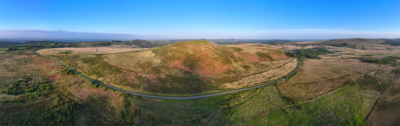 Aerial view of Chapelle Saint Michel de Brasparts on a grassy hill surrounded by moorland and a winding road under a clear blue sky Saint Rivoal Bretagne France. Aerial view of Chapelle Saint Michel de Brasparts on a grassy hill surrounded by moorland and a winding road under a clear blue sky Saint Rivoal Bretagne France.
