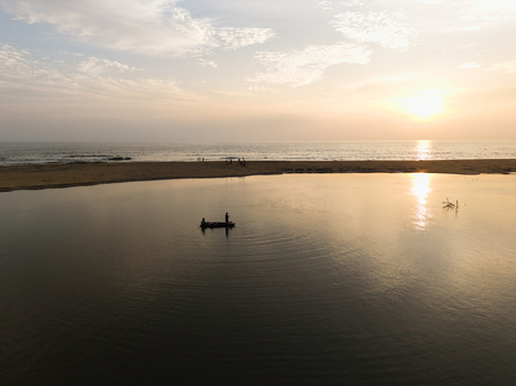 Aerial view of a small boat with fishermen on a calm lagoon during a golden sunset near the sandy beach in Galle Southern Province Sri Lanka. Aerial view of a small boat with fishermen on a calm lagoon during a golden sunset near the sandy beach in Galle Southern Province Sri Lanka.