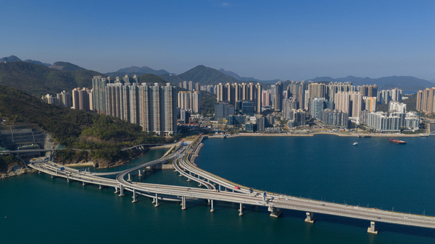 Aerial view of the modern cross bay bridge and highway connecting to a dense skyline of residential skyscrapers under a clear blue sky Hong Kong Hong Kong.
