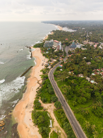 Aerial view of Dadalla beach with a winding coastal road crashing ocean waves and lush tropical greenery in Galle Southern Province Sri Lanka. Aerial view of Dadalla beach with a winding coastal road crashing ocean waves and lush tropical greenery in Galle Southern Province Sri Lanka.