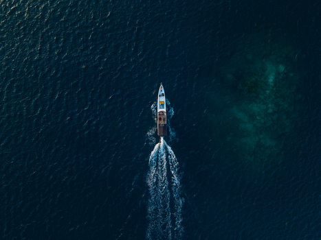 Aerial view of a small motorboat cruising through deep blue tropical waters leaving a white wake behind it near Karimunjawa Jawa Tengah Indonesia. Aerial view of a small motorboat cruising through deep blue tropical waters leaving a white wake behind it near Karimunjawa Jawa Tengah Indonesia.