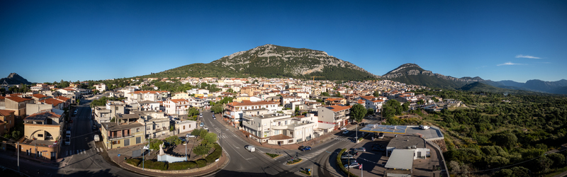 Aerial view of the town nestled at the base of rugged mountains with traditional rooftops and winding streets under a clear blue sky in Dorgali Sardinia Italy. Aerial view of the town nestled at the base of rugged mountains with traditional rooftops and winding streets under a clear blue sky in Dorgali Sardinia Italy.