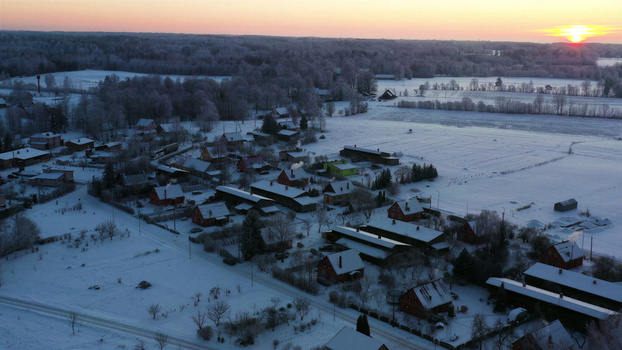 Aerial view of a snow covered rural village featuring small houses snow dusted trees and open fields under a soft morning sky Latvia. Aerial view of a snow covered rural village featuring small houses snow dusted trees and open fields under a soft morning sky Latvia.