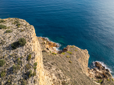 Aerial view of the rugged cliffs and rocky coastline of Cala Llebeig with Mediterranean vegetation overlooking the deep blue sea in El Poble Nou de Benitatxell Valencian Community Spain.