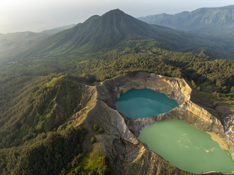 Aerial view of the turquoise and green crater lakes of Kelimutu National Park surrounded by lush volcanic mountains and dense forest in Detusoko East Nusa Tenggara Indonesia.