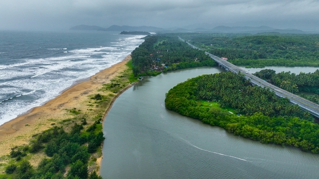 Aerial view of Galgibaga Beach where the river meets the Arabian Sea featuring a bridge crossing the water lush tropical vegetation and sandy coastline in Canacona Goa India.