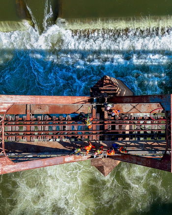 Aerial view of construction workers in high visibility gear working on a rusted steel railway bridge above a rushing river with white water rapids in Durban KwaZulu Natal South Africa.