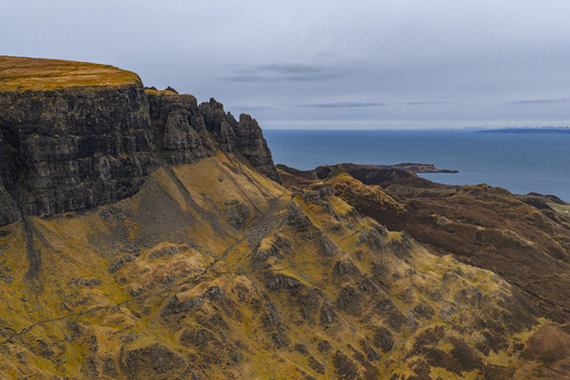 Aerial view of the dramatic rock formations and steep cliffs of The Quiraing overlooking the sea under a cloudy sky in the Isle of Skye Scotland United Kingdom. Aerial view of the dramatic rock formations and steep cliffs of The Quiraing overlooking the sea under a cloudy sky in the Isle of Skye Scotland United Kingdom.