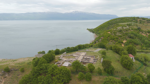 Aerial view of the archaeological ruins of the Lin Peninsula basilica overlooking the calm waters of Lake Ohrid with distant mountains in Lin Korce County Albania.