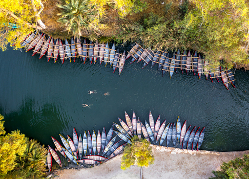 Aerial view of boats lining the tranquil river s edge where swimmers glide amidst the embrace of lush sun kissed foliage Kineret Israel.