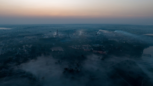 Aerial view of an industrial plant with smoking chimneys surrounded by morning mist and lush greenery near a river in Nagda Madhya Pradesh India. Aerial view of an industrial plant with smoking chimneys surrounded by morning mist and lush greenery near a river in Nagda Madhya Pradesh India.