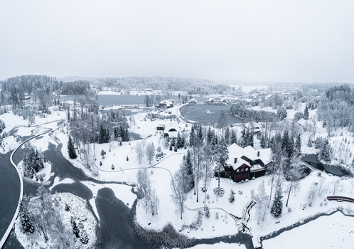 Aerial view of a snow covered landscape featuring a large wooden lodge nestled among frozen lakes and dense pine forests under a winter sky Latvia. Aerial view of a snow covered landscape featuring a large wooden lodge nestled among frozen lakes and dense pine forests under a winter sky Latvia.