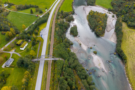 Aerial view of the Rauma river flowing through a lush rural landscape with a bridge crossing the road and railway tracks in Andalsnes More og Romsdal Norway.