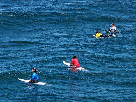 Aerial view of surfers in colorful wetsuits waiting for waves on their boards at Praia do Areal de Santa Barbara in Ribeira Grande Acores Portugal. Aerial view of surfers in colorful wetsuits waiting for waves on their boards at Praia do Areal de Santa Barbara in Ribeira Grande Acores Portugal.