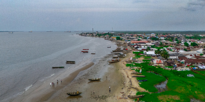 Aerial view of Bonny Island coastline featuring traditional wooden fishing boats on the sandy shore adjacent to a coastal town in Bonny Rivers Nigeria.