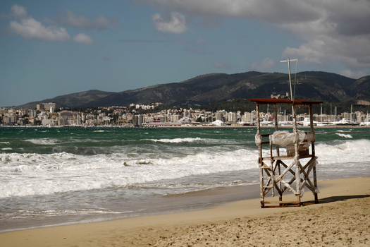 View of a lifeguard tower on the beach in Mallorca with the city skyline and mountains in the background in Balearic Islands Spain.