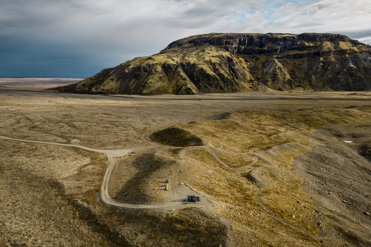 Aerial view of the rugged volcanic landscape near Vatnajokull with moss covered hills a winding dirt road and a small vehicle parked in the vast Icelandic wilderness Iceland.