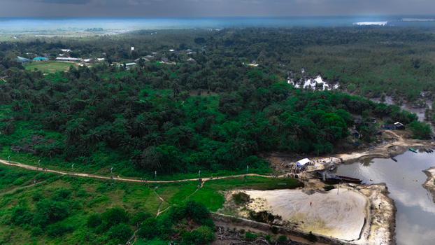 Aerial view of Bukuma in the Niger Delta featuring lush tropical vegetation a winding riverbank small wooden boats and a sandy landing area in Buguma Rivers Nigeria.