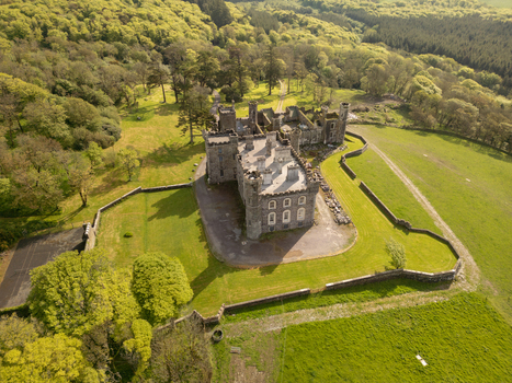 Aerial view of Castlefreke Castle surrounded by lush green fields stone walls and dense woodland in Castlefreke County Cork Ireland.