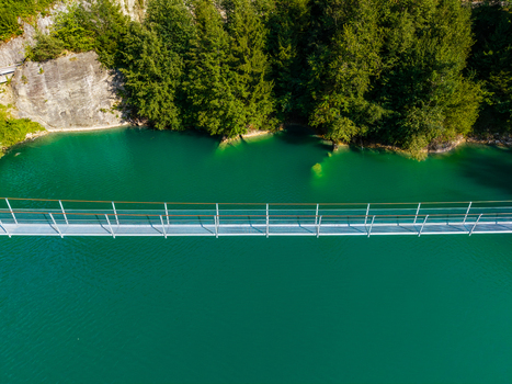 Aerial view of the suspension bridge over the turquoise waters of the Lac de la Gruyere near the Barrage de Rossens surrounded by trees and cliffs in Pont la Ville Fribourg Switzerland.