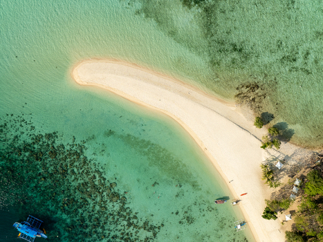 Aerial view of Malcapuya Island featuring a pristine white sand beach vibrant turquoise waters coral reefs and small boats anchored in Coron Mimaropa Philippines. Aerial view of Malcapuya Island featuring a pristine white sand beach vibrant turquoise waters coral reefs and small boats anchored in Coron Mimaropa Philippines.