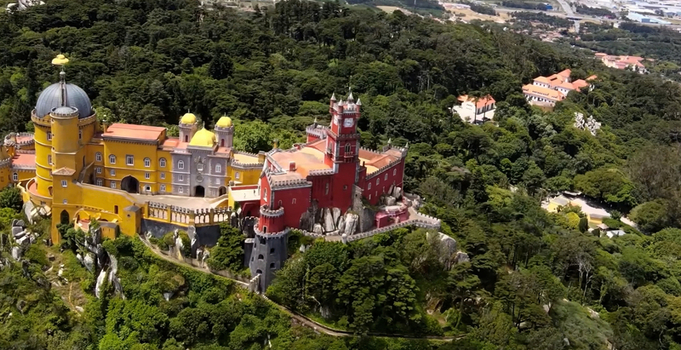 Aerial view of the National Palace of Pena with its vibrant yellow and red towers set amidst the lush green forests and rocky hills of Sintra Lisboa Portugal. Aerial view of the National Palace of Pena with its vibrant yellow and red towers set amidst the lush green forests and rocky hills of Sintra Lisboa Portugal.