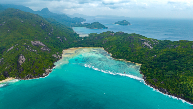 Aerial view of the turquoise waters and coral reefs of Cap Ternay surrounded by lush green hills and rocky coastline Cap Ternay Port Glaud Seychelles. Aerial view of the turquoise waters and coral reefs of Cap Ternay surrounded by lush green hills and rocky coastline Cap Ternay Port Glaud Seychelles.