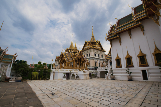 View of The Grand Palace with ornate golden spires and traditional Thai architecture under a cloudy sky in Bangkok Thailand. View of The Grand Palace with ornate golden spires and traditional Thai architecture under a cloudy sky in Bangkok Thailand.