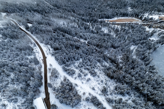Aerial view of Mummelsee surrounded by a dense snow covered forest and a winding road in Seebach Baden Wurttemberg Germany. Aerial view of Mummelsee surrounded by a dense snow covered forest and a winding road in Seebach Baden Wurttemberg Germany.