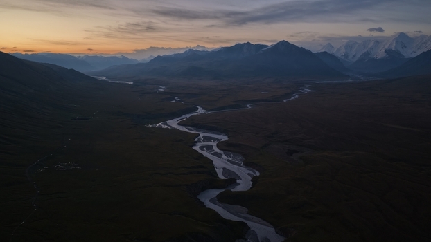 Aerial view of Engilchek Glacier with a winding river flowing through the valley surrounded by snow capped mountains under a twilight sky in Ak Su Issyk Kul Region Kyrgyzstan. Aerial view of Engilchek Glacier with a winding river flowing through the valley surrounded by snow capped mountains under a twilight sky in Ak Su Issyk Kul Region Kyrgyzstan.