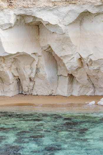 View of white limestone cliffs overlooking a small sandy beach and crystal clear turquoise water in Syracuse Sicily Italy.