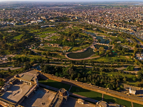 Aerial view of the historic Minar e Pakistan and surrounding lush green park with winding pathways and water features set against the dense urban landscape of Lahore Punjab Pakistan.
