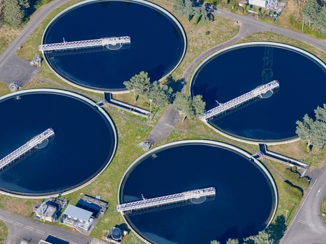 Aerial view of four circular water treatment tanks with bridges over deep blue water nestled among green fields and buildings Sausheim Grand Est France.