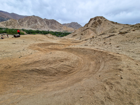 View of a winding dirt track through the arid desert landscape with rugged mountains in the background under a cloudy sky in Leh Ladakh India.