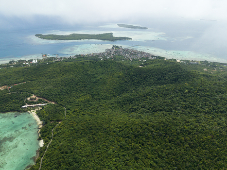 Aerial view of lush green forests meeting the turquoise sea with the settlement nestled atop framed by distant islands Karimunjawa Central Java Indonesia.