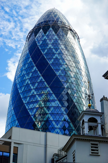 View of 30 St Mary Axe also known as The Gherkin featuring its iconic glass facade and geometric structure against a blue sky in London England United Kingdom.
