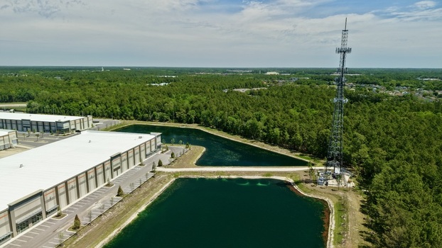 Aerial view of a large industrial warehouse and a tall telecommunications tower next to retention ponds and dense green forest in World Golf Village Florida United States. Aerial view of a large industrial warehouse and a tall telecommunications tower next to retention ponds and dense green forest in World Golf Village Florida United States.